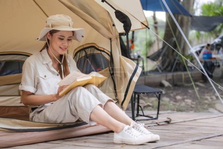 Téléchargez les photos : Jeune touriste dans la trentaine en vêtements safari assise dans une tente de camping et lisant un livre, activité de voyage en plein air Détendez-vous au milieu de la nature. - en image libre de droit