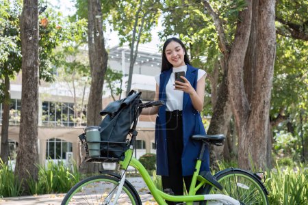 Foto de Hermosa mujer joven con teléfono inteligente utiliza la aplicación de alquiler de bicicletas de la ciudad servicio de intercambio de bicicletas para reducir la contaminación del aire.. - Imagen libre de derechos