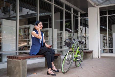 Asiatische Geschäftsfrau fährt mit dem Fahrrad in die Stadt, um außerhalb der Stadt zu arbeiten, um die Kohlendioxidemissionen zu reduzieren. Alternative Transportmittel für grüne Energie.