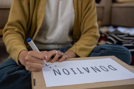 Eine schöne Asiatin benutzt einen magischen Marker, um auf eine Schachtel Kleidung zu schreiben, die gespendet wird, um moralische Unterstützung zu zeigen..