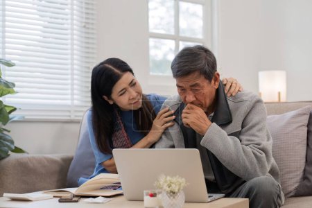 Una pareja asiática jubilada se sienta estresada mientras calculan sus gastos mensuales en el sofá de la sala..