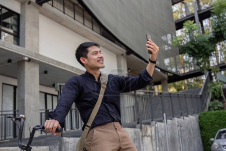 Ein junger asiatischer Geschäftsmann fährt mit dem Fahrrad zur Arbeit. Draußen vor dem Büro stehen, telefonieren und über Geschäfte reden. Konzept zur Verringerung von Energie und Luftverschmutzung..