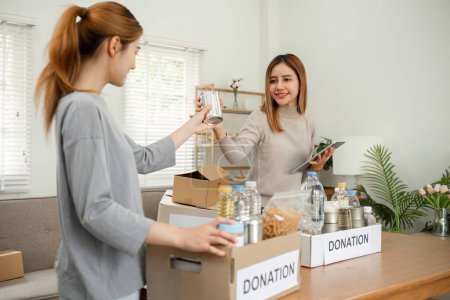 Photo for Two young female volunteers help pack food into donation boxes and prepare to donate them to charity.. - Royalty Free Image
