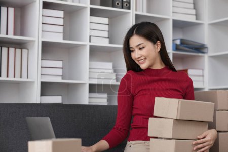 Femme entrepreneur emballage produits pour les ventes en ligne, travaillant sur ordinateur portable dans un bureau moderne avec des étagères.