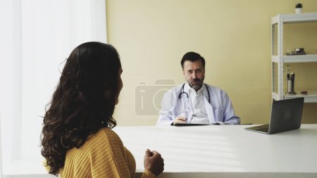 Doctor patient medical concept Caucasian and Latin consulting talking at table with notebook.