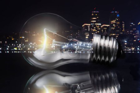 Photo for Close up of tungsten light bulb with glow on dark background and night city lights - Royalty Free Image