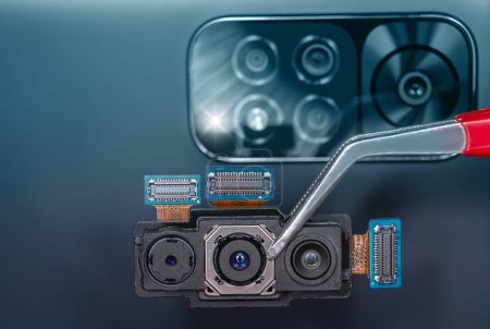 Téléchargez les photos : Gros plan de la triple caméra d'un smartphone tenue avec une pince à épiler - en image libre de droit