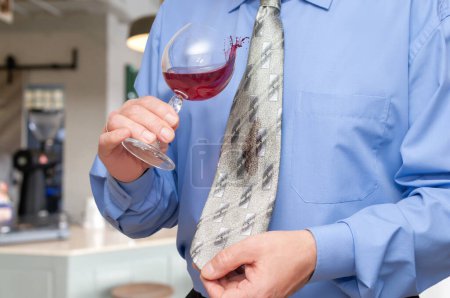 Photo for A man holding a wine glass in his hand and is letting some of vine drip onto his tie. - Royalty Free Image