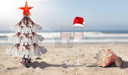 Photo for Concept of Christmas and New Year celebrations in tropical countries. Stylised Christmas tree made of coral and starfish, shells and wine glasses on the seashore. - Royalty Free Image