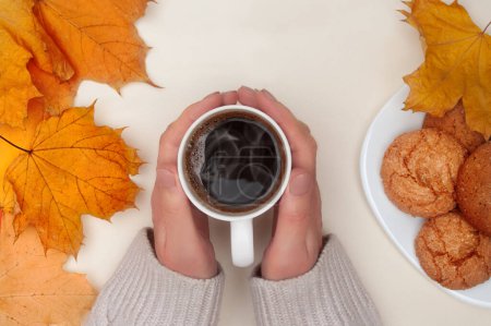 Photo for Flat lay of autumn yellow maple leafs, woman's hands hold cup of hot tea and white plate with cookies on ivory background. Top view. - Royalty Free Image