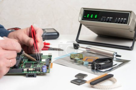 Photo for Close up of a technician's hands in a workshop. Repairer is soldering circuit board of electronic device on table with tweezers. - Royalty Free Image