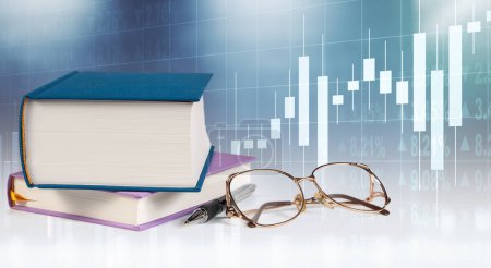 A collection of books is piled next to office supplies including pens and glasses, all set against the backdrop of an illuminated stock market graph.