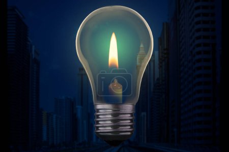 Light bulb with candle burning inside against a modern city district without electricity at night. Emergency blackout concept.