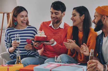 Téléchargez les photos : Beau jeune homme tenant gâteau d'anniversaire tout en célébrant avec des amis - en image libre de droit