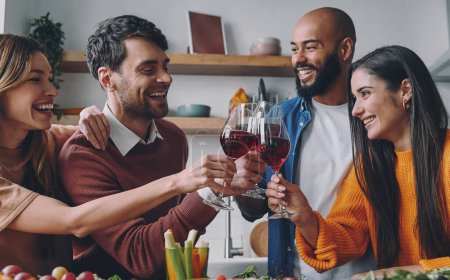 Téléchargez les photos : Jeunes gens joyeux griller avec du vin tout en dînant à la maison ensemble - en image libre de droit