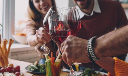 Close-up of happy young people toasting with wine while having dinner at home together