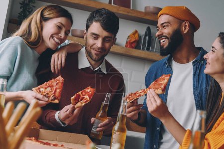 Téléchargez les photos : Groupe de jeunes mangeant de la pizza et souriant tout en profitant du plaisir ensemble - en image libre de droit