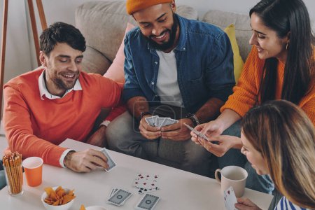 Foto de Vista superior de los jóvenes jugando a las cartas y sonriendo mientras disfrutan de un tiempo sin preocupaciones juntos - Imagen libre de derechos