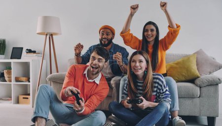 Photo for Beautiful young people playing video games and smiling while enjoying carefree time together - Royalty Free Image