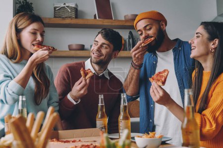 Foto de Jóvenes alegres comiendo pizza y sonriendo mientras disfrutan de momentos divertidos juntos - Imagen libre de derechos
