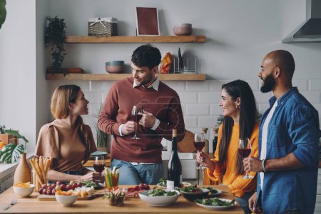 Téléchargez les photos : Beaux jeunes gens parlant et souriant tout en profitant du dîner à la maison ensemble - en image libre de droit