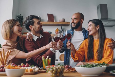 Téléchargez les photos : Heureux les jeunes qui trinquent avec du vin tout en dînant ensemble à la maison - en image libre de droit