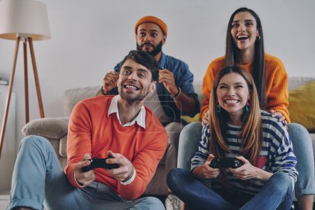Photo for Group of young people playing video games and smiling while enjoying carefree time together - Royalty Free Image