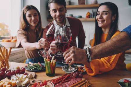 Téléchargez les photos : Heureux les jeunes qui trinquent avec du vin tout en dînant ensemble à la maison - en image libre de droit