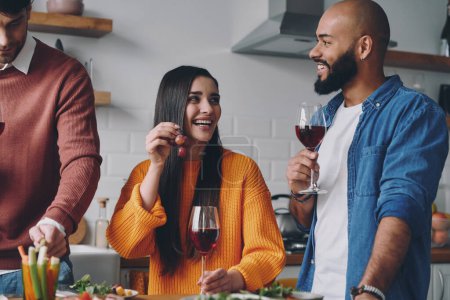 Téléchargez les photos : Jeunes gens joyeux profitant de la nourriture et des boissons tout en dînant à la maison ensemble - en image libre de droit