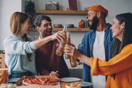 Foto de Grupo de jóvenes felices brindando con cerveza mientras disfrutan de la pizza juntos - Imagen libre de derechos