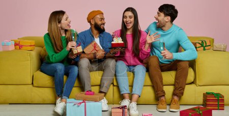 Photo for Young people congratulating friend with birthday while sitting on the couch against pink background - Royalty Free Image