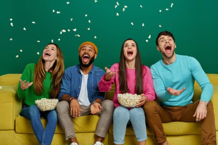 Photo for Group of cheerful young people throwing popcorn while sitting on the couch against pink background - Royalty Free Image