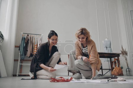 Téléchargez les photos : Deux créatrices de mode heureuses planifiant une nouvelle collection en atelier ensemble - en image libre de droit