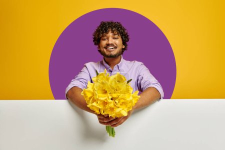 Téléchargez les photos : Heureux homme indien étirant bouquet de fleurs sur fond jaune - en image libre de droit