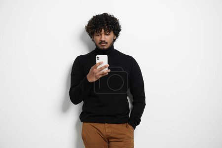 Foto de Hombre indio guapo usando el teléfono inteligente mientras está de pie contra el fondo - Imagen libre de derechos