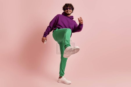 Photo for Playful young Indian man stretching out leg while dancing against pink background - Royalty Free Image