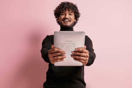 Photo for Handsome Indian man holding digital tablet and smiling against pink background - Royalty Free Image