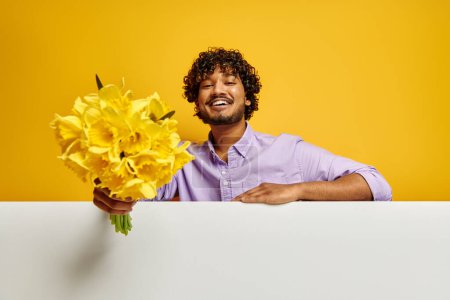 Photo for Handsome Indian man stretching out flower bouquet against yellow background - Royalty Free Image