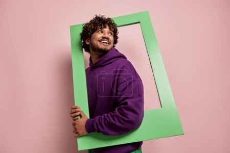Foto de Hombre indio alegre mirando fuera del marco de la imagen mientras está de pie sobre el fondo rosa - Imagen libre de derechos