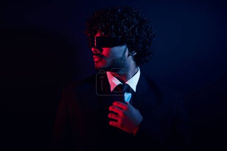 Photo for Confident businessman in futuristic glasses adjusting his necktie against black background - Royalty Free Image