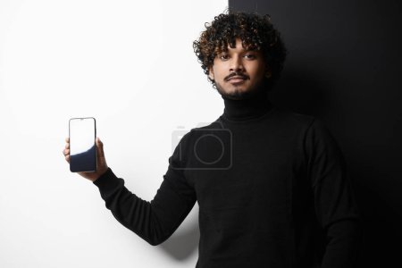 Téléchargez les photos : Bel homme indien tenant téléphone intelligent sur fond noir et blanc - en image libre de droit