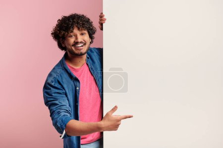 Foto de Guapo joven indio apuntando espacio de copia y sonriendo sobre fondo rosa - Imagen libre de derechos