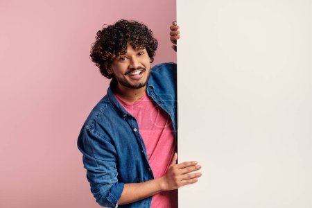 Foto de Feliz joven indio apoyado en el espacio de copia mientras está de pie sobre el fondo rosa - Imagen libre de derechos