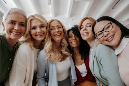 Tiefer Blickwinkel auf eine multiethnische Gruppe reifer Frauen, die sich umarmen und in die Kamera lächeln