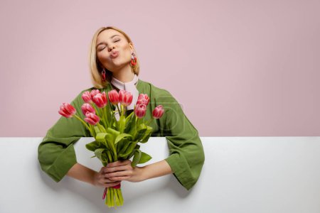 Foto de Hermosa joven sosteniendo racimo de tulipanes y sonriendo sobre fondo rosa - Imagen libre de derechos