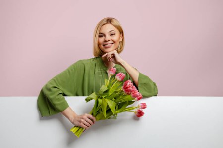 Téléchargez les photos : Heureuse jeune femme aux cheveux blonds tenant un bouquet de tulipes sur fond rose - en image libre de droit