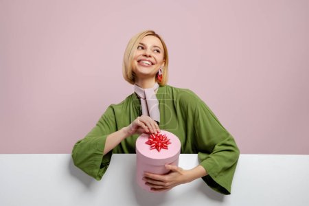 Foto de Atractiva joven mujer sosteniendo una caja de regalo y sonriendo sobre fondo rosa - Imagen libre de derechos