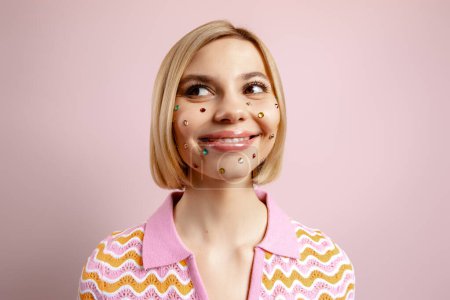 Foto de Mujer joven feliz con diamantes de imitación de colores sobre su cara de pie sobre el fondo rosa - Imagen libre de derechos