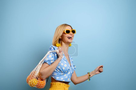 Foto de Bolso de malla de mujer joven de moda con naranjas en el hombro contra fondo azul - Imagen libre de derechos