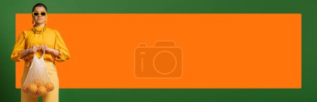 Téléchargez les photos : Jeune femme à la mode aux cheveux courts portant un sac en filet avec des oranges sur fond vert - en image libre de droit